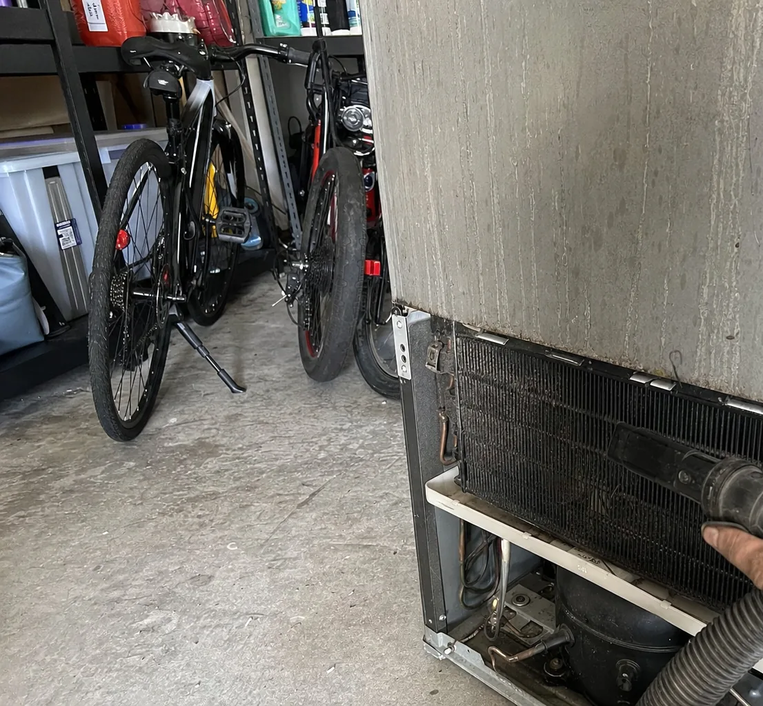 A refrigerator standing beside bicycles and plastic storage bins on a bare concrete garage slab.