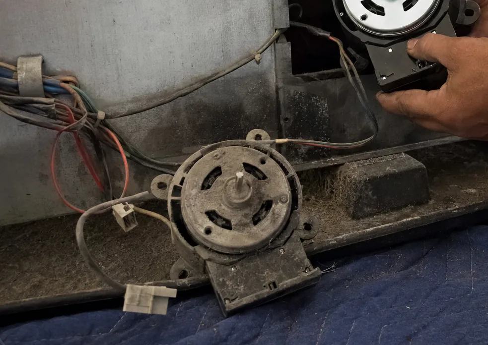 A wiring harness and its connectors behind an opened service panel, with a fan motor set down on the blanket below.